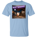 A light blue short-sleeve t-shirt with a colorful graphic print of a Halloween night scene featuring cat's going trick or treating, and a cat jumping out from behind a tree, dressed as a ghost, to scare the other cats, and the text 'BOO - YAAAAAH!!' in purple neon, worn by a model. The cat that was the intended target is holding up it's middle finger under it's costume as an automatic response to the annoying ghost.