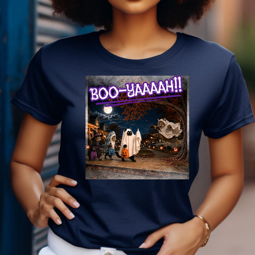 A navy blue short-sleeve t-shirt with a colorful graphic print of a Halloween night scene featuring cat's going trick or treating, and a cat jumping out from behind a tree, dressed as a ghost, to scare the other cats, and the text 'BOO - YAAAAAH!!' in purple neon, worn by a model. The cat that was the intended target is holding up it's middle finger under it's costume as an automatic response to the annoying ghost.