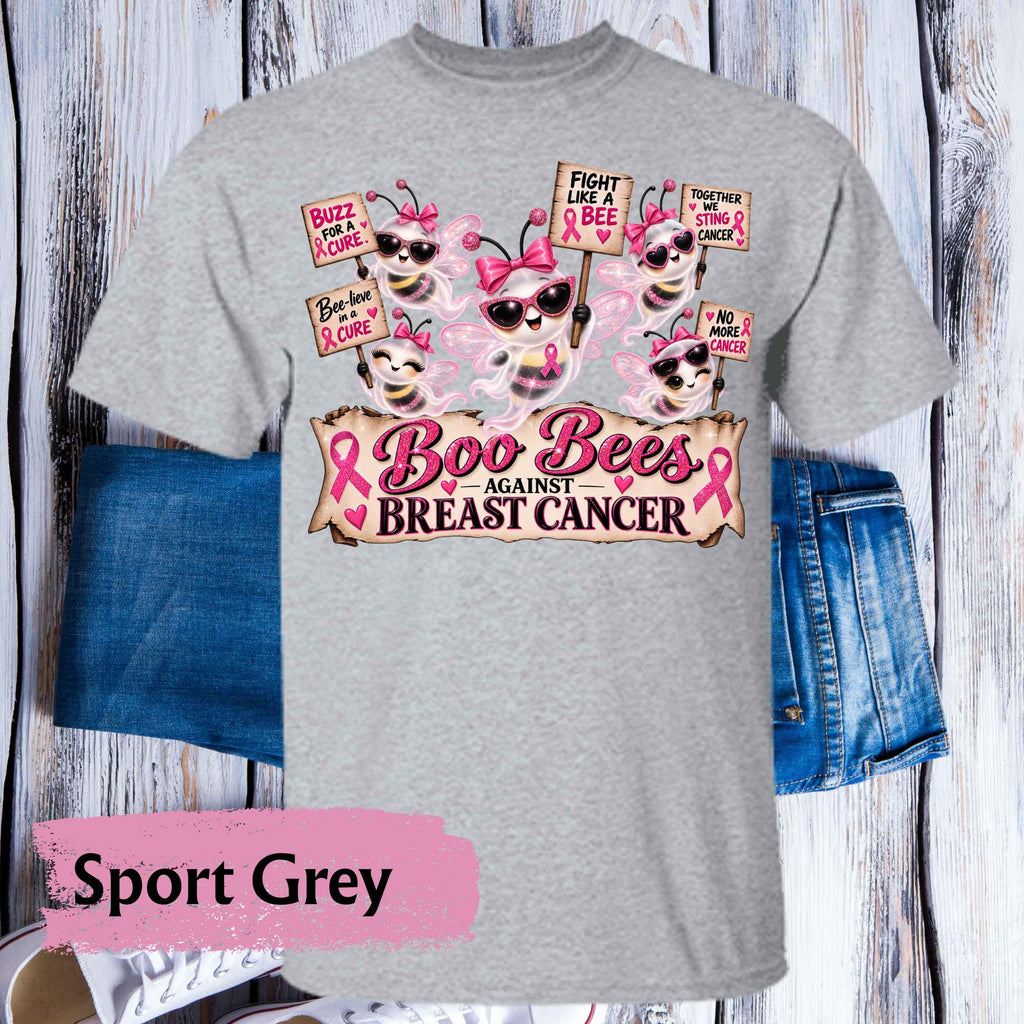 A heather grey short-sleeve t-shirt with a 'Boo Bees Against Breast Cancer' graphic print, styled flat on a white wood plank background with blue denim shorts and a pink 'Sport Grey' label overlay.