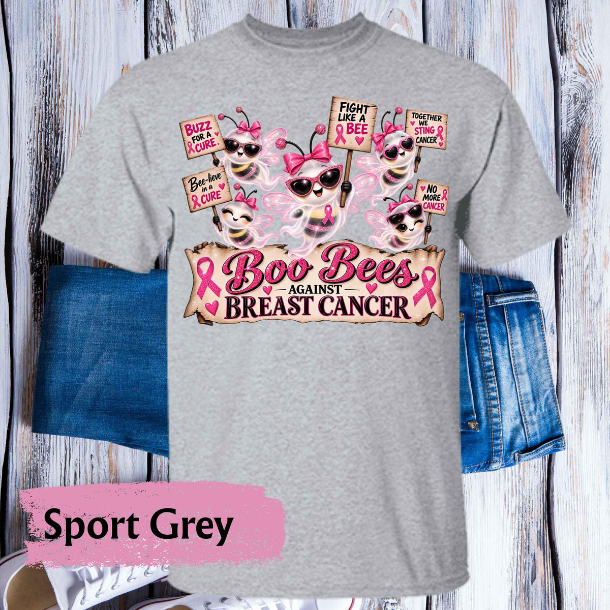 A heather grey short-sleeve t-shirt with a 'Boo Bees Against Breast Cancer' graphic print, styled flat on a white wood plank background with blue denim shorts and a pink 'Sport Grey' label overlay.