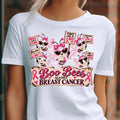 A white short-sleeve graphic T-shirt worn by a model, featuring cartoon bees in pink sunglasses holding breast cancer awareness signs with the text 'Boo Bees Against Breast Cancer' and pink ribbons.