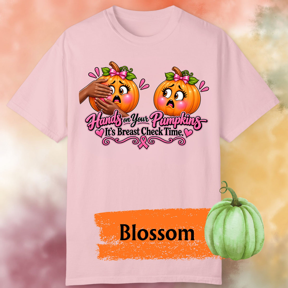 A light pink short-sleeve t-shirt with a playful Breast Cancer Awareness Halloween design featuring two adorably horrified pumpkins, pink bows, pink accents, a breast cancer awareness ribbon and the cheeky reminder: “Hands on Your Pumpkins — It's Breast Check Time!” One of the pumpkins is being squeezed.