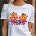 A white short-sleeve graphic t-shirt worn by a model, featuring a humorous  important reminder with this funny Breast Cancer Awareness Shirt, created for women who like their Pink October message with a little sass. This playful Breast Cancer Awareness Halloween design features two adorably horrified pumpkins, pink bows, pink accents, a breast cancer awareness ribbon and the cheeky reminder: “Hands on Your Pumpkins — It's Breast Check Time!” while what hands are squeezing the one pumpkin for lumpkins.