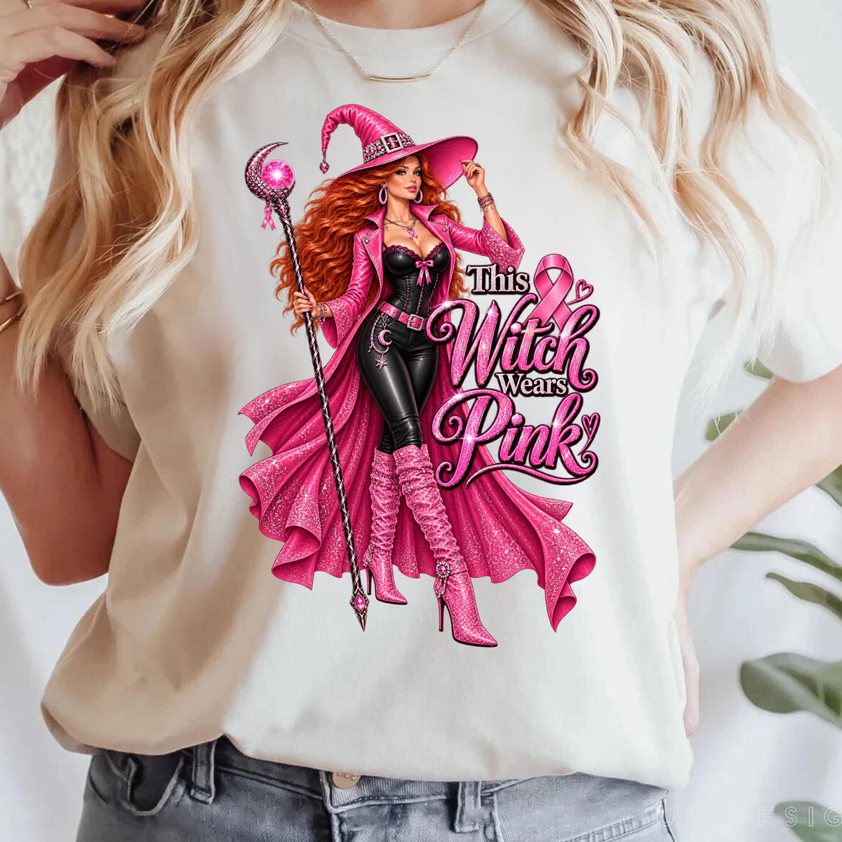 A model wearing a white t-shirt with a graphic making a bold statement for Breast Cancer Awareness Month with this glamorous pink witch Breast Cancer Awareness shirt featuring a fierce redheaded witch dressed head-to-toe in sparkling pink and black, complete with a pink ribbon necklace, magical staff, rhinestone-covered witch hat and enough attitude to put a spell on cancer itself. The statement “This Witch Wears Pink” turns classic Halloween style into a fun, unapologetic show of support. 