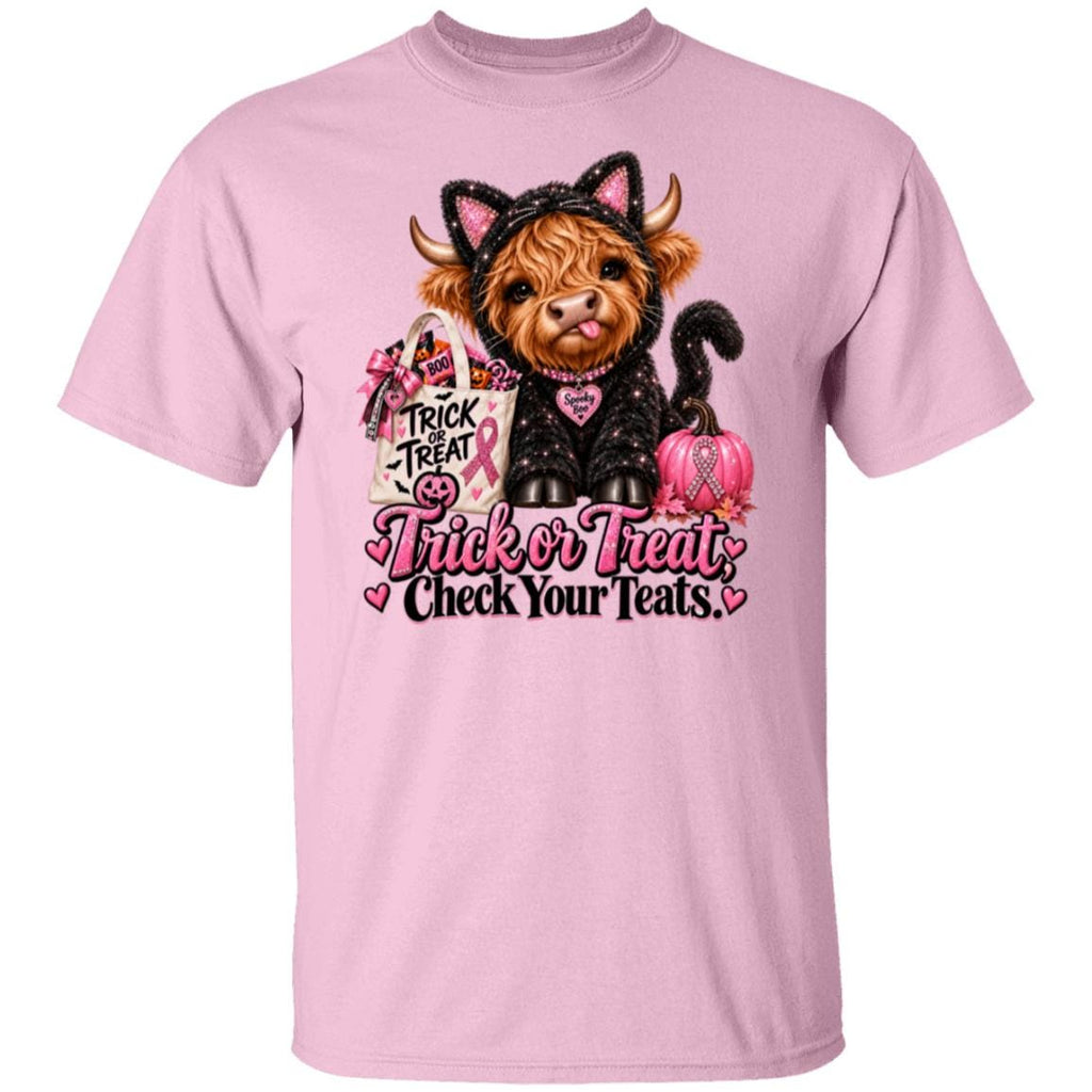 A light pink short-sleeve crewneck t-shirt featuring a graphic of a Scottish highland cow dressed in a black cat costume with pink accents, holding a pink pumpkin and a bag that reads 'Trick or Treat'. Below the cow is the text 'Trick or Treat Check Your Teats' in pink and black lettering.