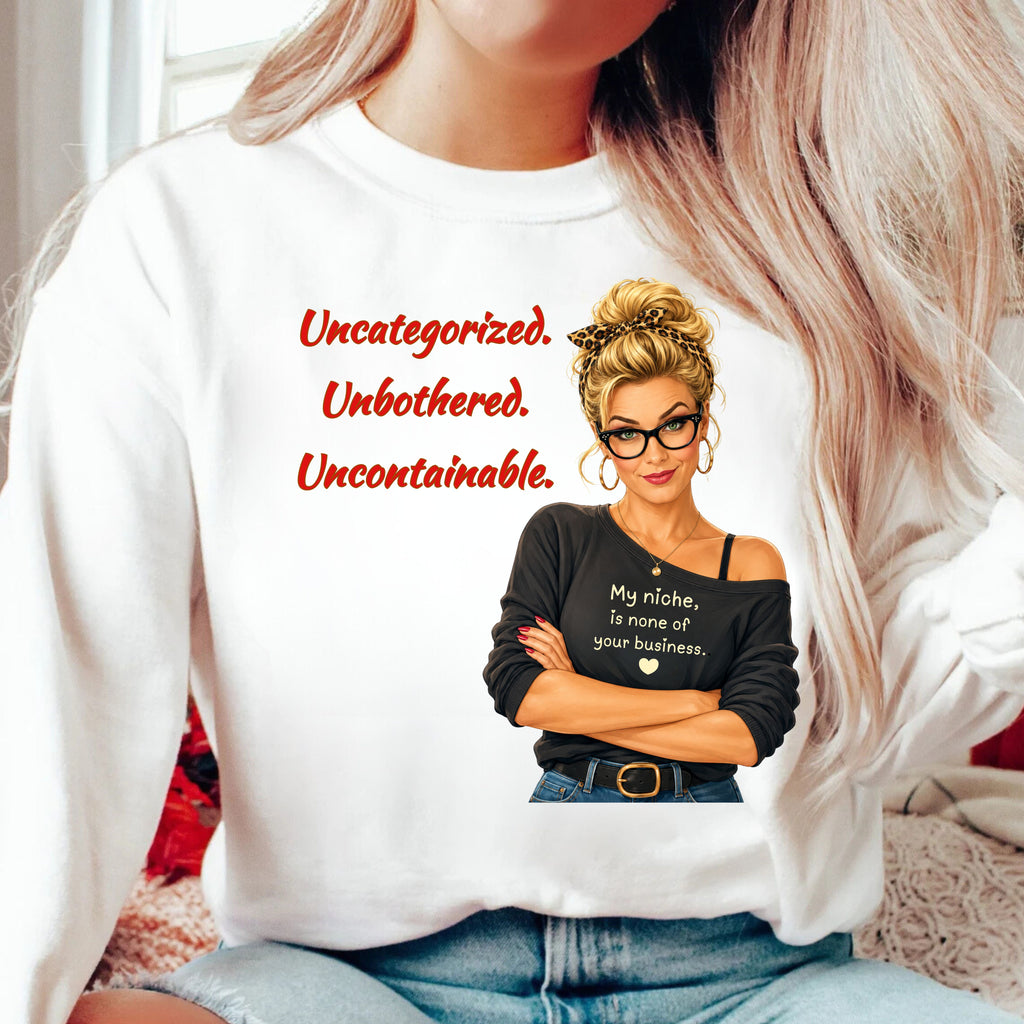 A confident, stylish woman with a playful go ahead, try to categorize me expression, wearing a white sweatshirt with a graphic design.  This design pairs “Uncategorized. Unbothered. Uncontainable.” with the perfectly cheeky declaration:

“My niche is none of your business."