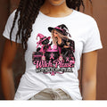 A model wearing a white short sleeved t-shirt with a design featuring a glamorous witch and her sassy black-cat sidekick brewing up something far more important than your average Halloween potion. Surrounded by sparkling pink breast cancer ribbons, pink pumpkins and bottles of Faith and Fight, their cauldron is bubbling with one mission: Finding a cure. The black cat is throwing up a hold it paw to the witch and the words say "Witch Please. We've got a cure to find."