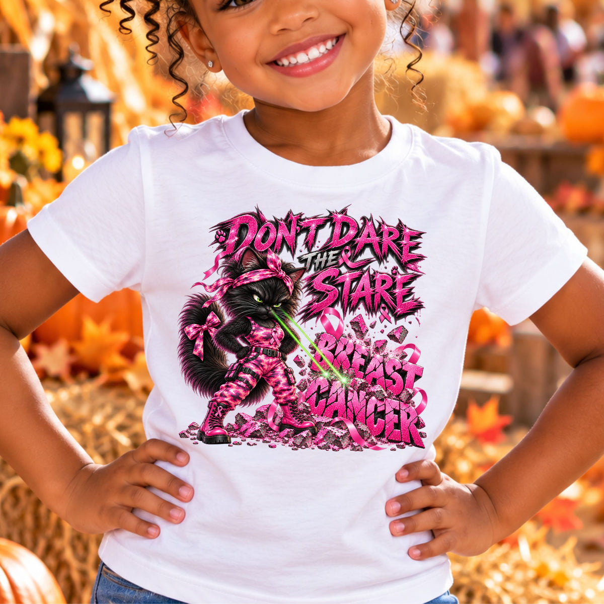 A smiling young girl wearing a white graphic t-shirt featuring a graphic with one seriously fierce black cat dressed for battle in sparkling pink camo, bright pink combat boots and breast cancer ribbons. She's standing with her paws on her hips, giving breast cancer THE STARE—and apparently that stare is powerful enough to blast BREAST CANCER into a pile of rubble. Featuring the fun phrase: “DON'T DARE THE STARE".