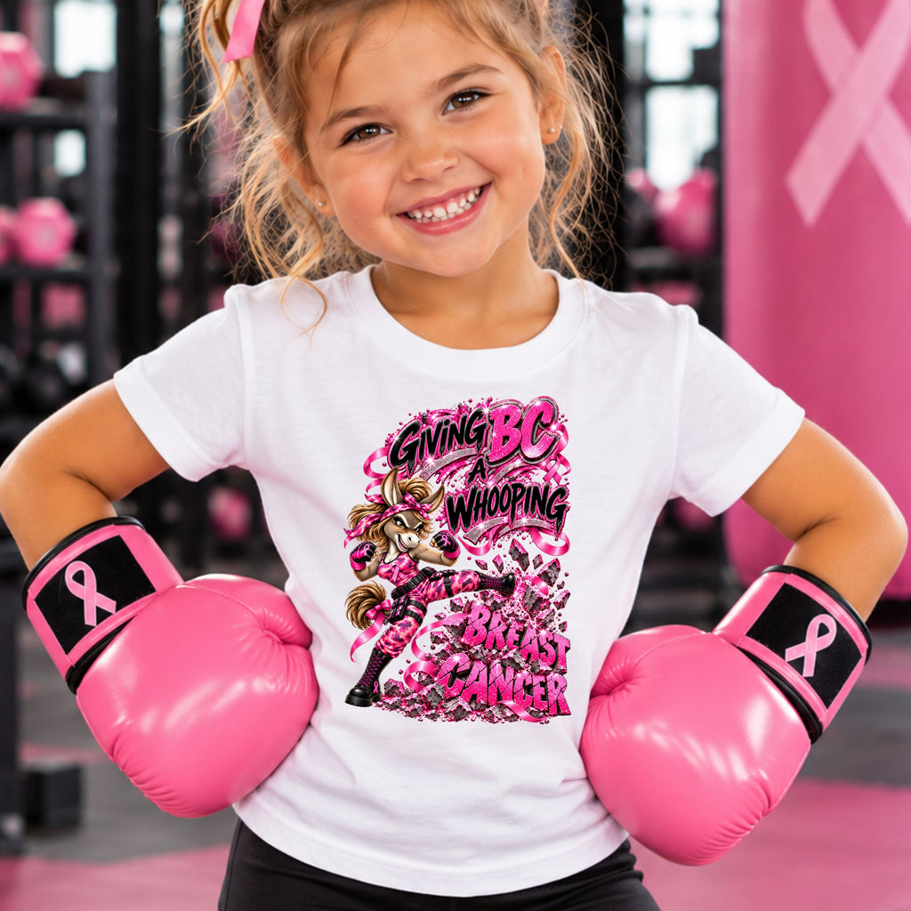 A young girl wearing a white graphic T-shirt and pink boxing gloves in a pink-themed setting. The shirt features a bold graphic of a fierce donkey kicking the words BREAST CANCER, with the text "GIVING BS A WHOPPING".
